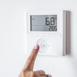 A right pointer finger getting ready to press a button on a white digital thermostat showing 68 degrees