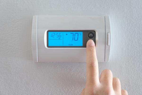 A pointer finger pressing the down arrow on a thermostat that is displaying 70 degrees