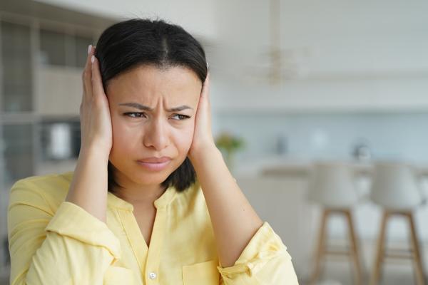 Woman wearing a yellow button up shirt, using both of her hands to cover both of her ears.