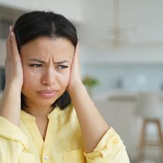 Woman wearing a yellow button up shirt, using both of her hands to cover both of her ears.