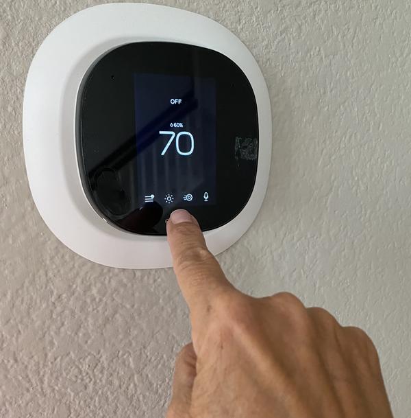A right pointer finger touching the screen of a smart thermostat