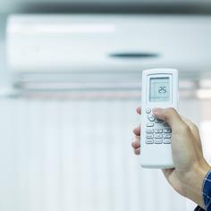 A right hand holding a remote up and pointed towards a ductless AC wall unit