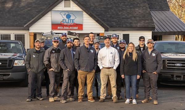 The Elite Air and Heat team standing in front of their business building and service vehicles.