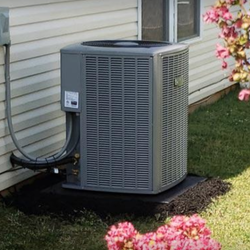 Ground AC unit sitting on a grassy lawn surrounded by pink flowers.