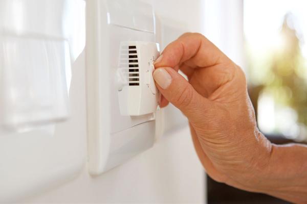 A close of a person's hand adjusting a plastic white thermostat built into a white wall.
