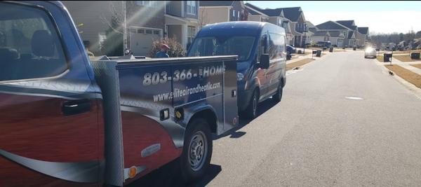An Elite Air service truck and service van parked out on the road in front of some two story homes.