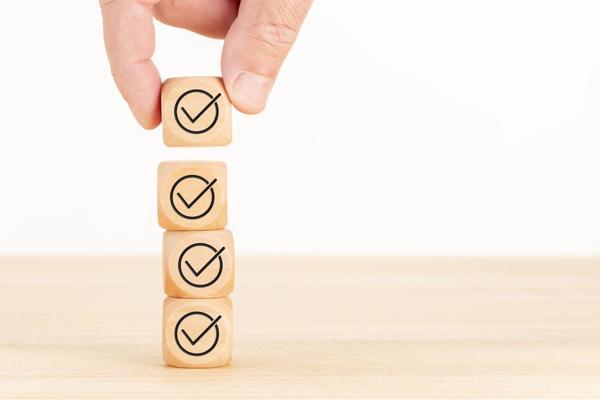 A hand that is stacking four small wooden cubes on top of each other that have a check mark surrounded by a circle printed on each of them.