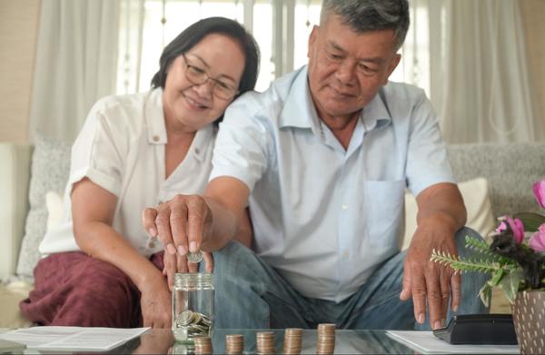 A couple sitting on their living room couch together, putting coins into a glass jar that is sitting on their glass coffee table.