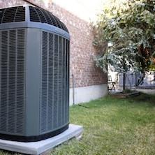An outdoor AC unit sitting on a concrete pad next to a brick wall and surrounded by a grassy lawn.