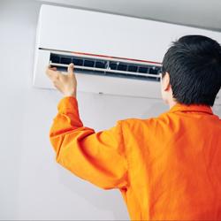Tech wearing an orange shirt adjusting the vent opening on a ductless AC unit affixed to a white wall.