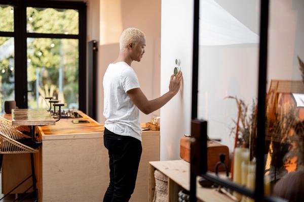 Man standing at his thermostat, adjusting the settings.