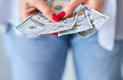 Woman with bright nail polish holding dollar bills in hand
